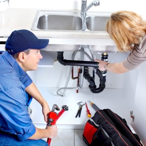 Mature plumber fixing a sink at kitchen